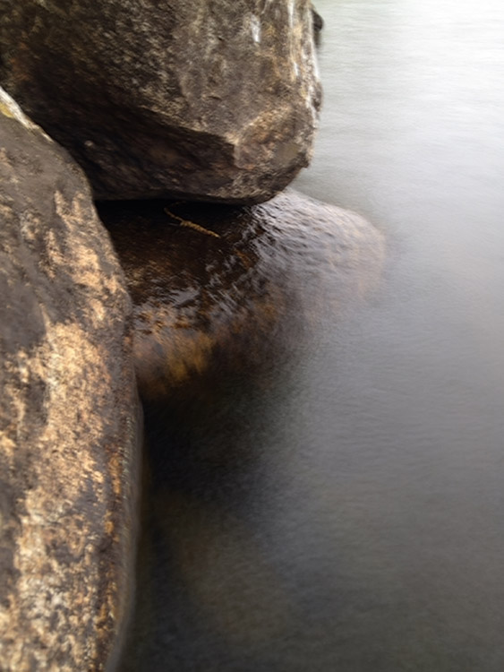 image of bolders on a lakeside with water smoothly washing over them